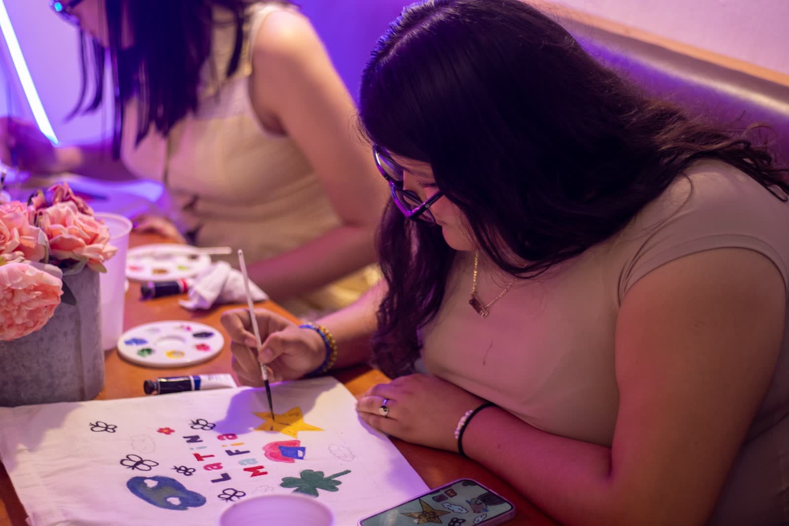 Asistentes pintando sus tote bags en una mesa de William's, con flores y paletas de colores
