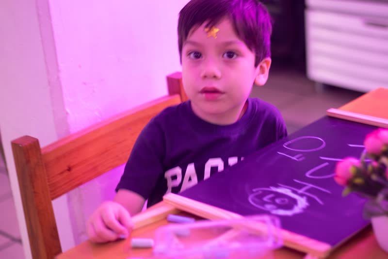 Pequeño artista mirando a la cámara junto a su pizarrón